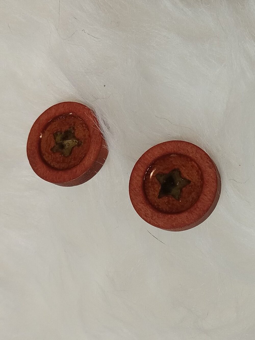 Handmade earrings on a wooden base with a piece of punched-out tree leaf
